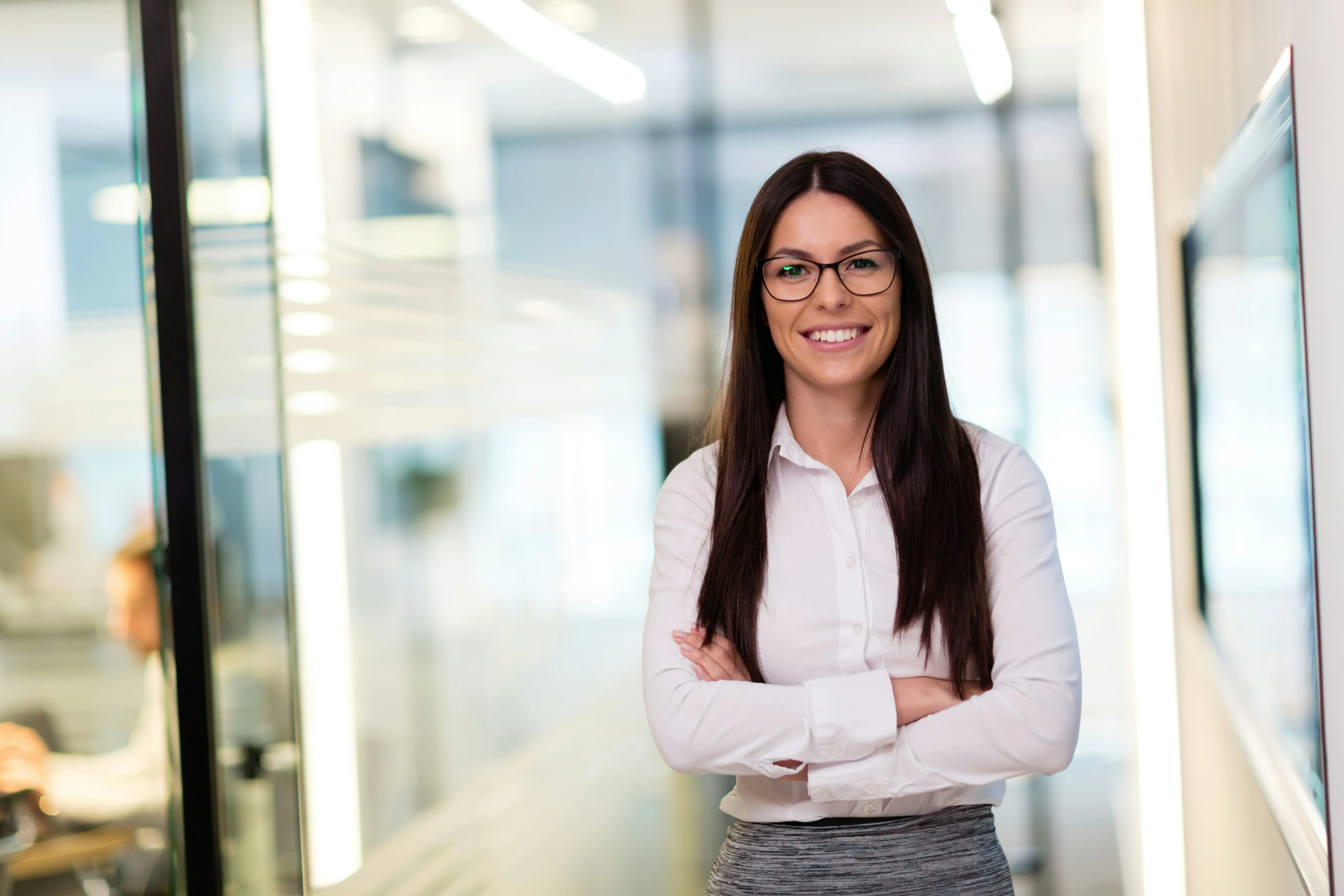 A temporary worker stands in an office corridor smiling with her arms crossed.